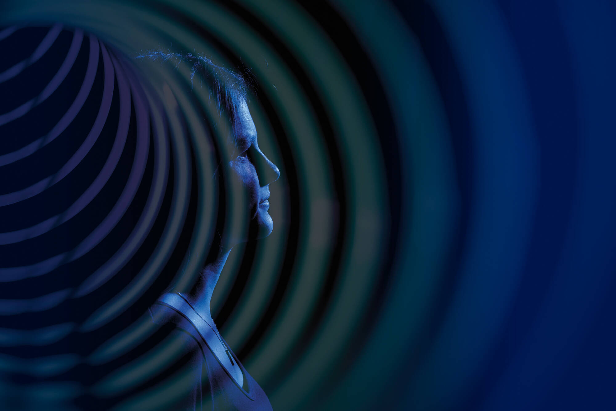 A student in profile against a dark background with dramatic blue lighting and ripples emanating in the foreground.